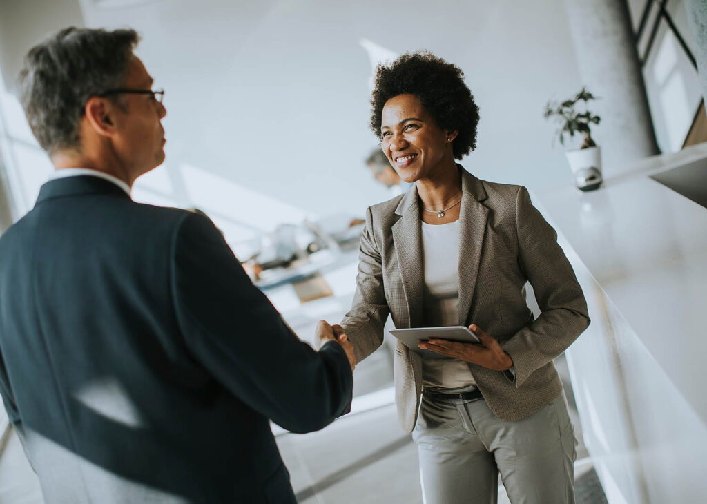 Businesswoman holding digital tablet and looking at colleague while shaking hands Businesswoman holding digital tablet and looking at colleague while shaking hands